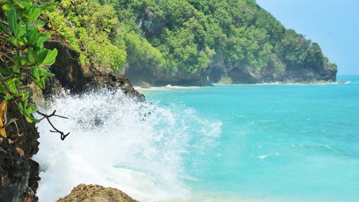 Suasana Pantai Pasir Putih dengan Bebatuan Karang Warna Hijau